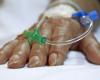 Photo of a surgery patient's hand resting on a bed, with tubes going into the hand