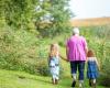 Woman in pink top walking, holding hands with two little girls, backs to camera, in a garden