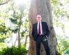 Paul Farmer stands against the front of a tall tree.