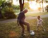 Caught in the middle of a one-on-one soccer game, a wite-haired man stands with his foot on a soccer ball, a small child faces him, poised to take the ball.