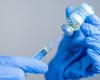 Hands in protective gloves putting a needle into a COVID-19 booster vaccine vial