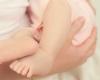 Photo of someone holding an infant, only the baby's feet and legs shown