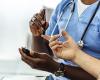 Health care provider in blue scrubs with stethoscope and darker skin tests the blood sugar of a light-skinned patient 