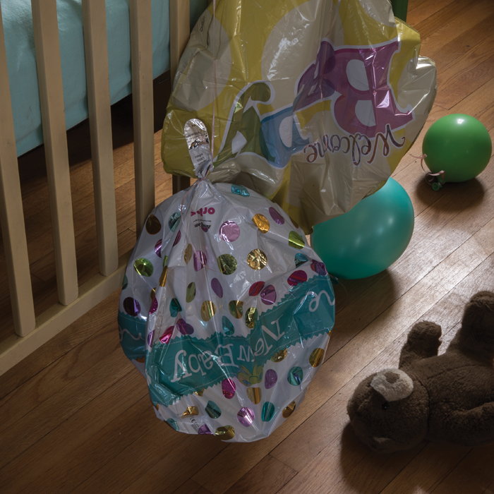 A crib with a deflated "welcome baby" balloon and teddy bear on floor nearby