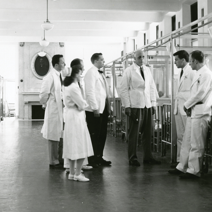 In this mid-twentieth century photo, William Bosworth Castle, MD 1921 (center) talks with medical staff and faculty in a ward at Boston City Hospital