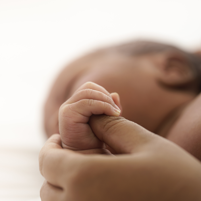 closeup of an infant whose hand is grasping the thumb of an adult
