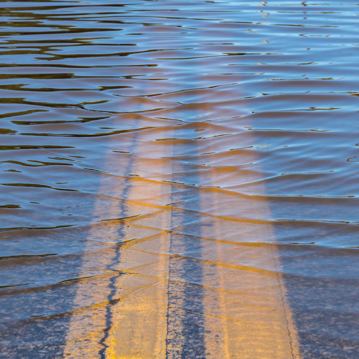 double yellow center lines of a roadway disappear into deep water