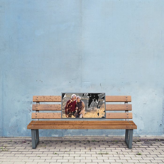 worn poster of older couple adorns the back of a park bench set against a blank wall 