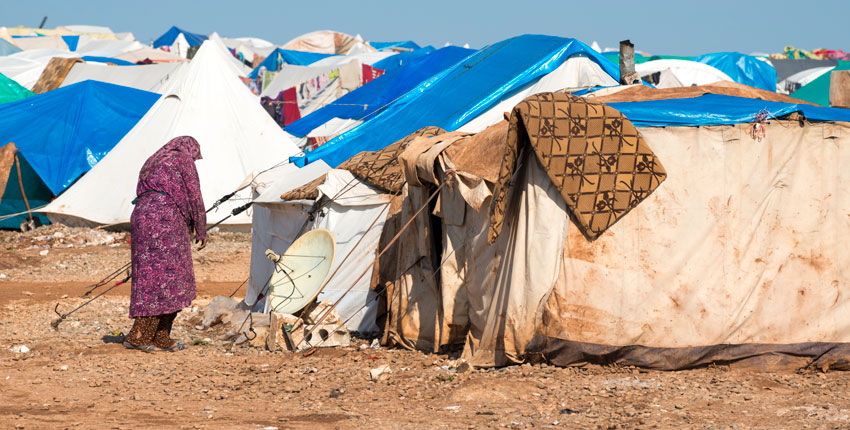 Image of a woman outside a makeshift tent in a Syrian refugee camp