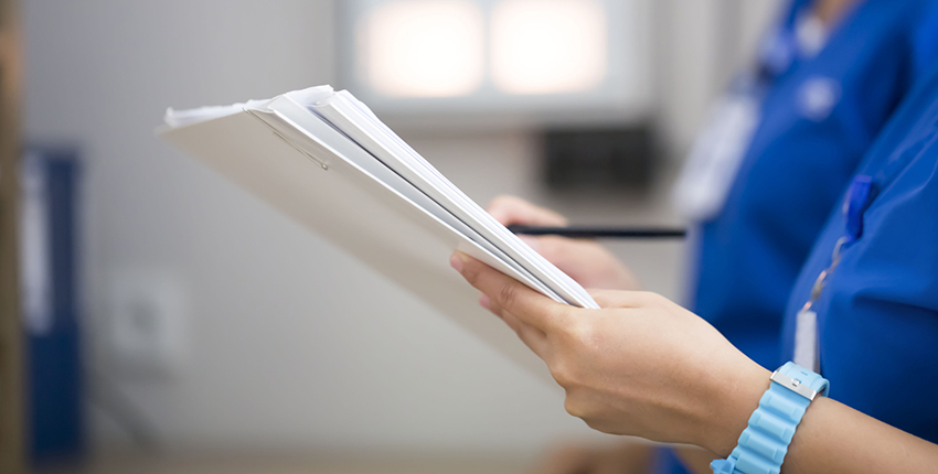 two people in scrubs, heads not shown, review a sheaf of papers indicating a patient file