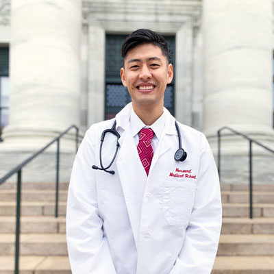 Photo of Inkyu Kim in front of HMS's Gordon Hall in white coat