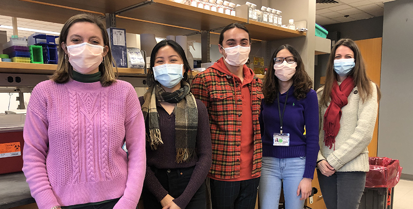 Five people in masks smile at the camera in front of a lab bench