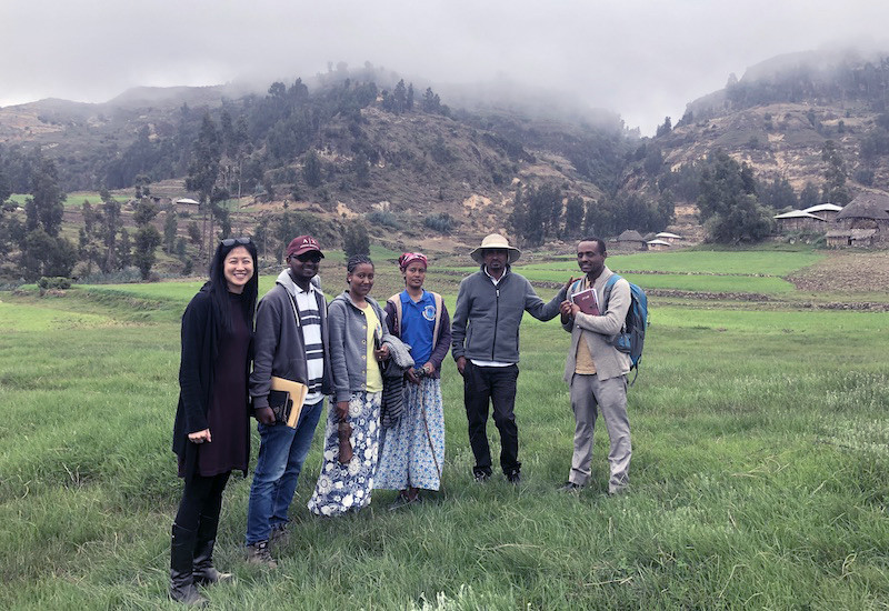 Chan and five colleagues stand in a field with mountains in the background