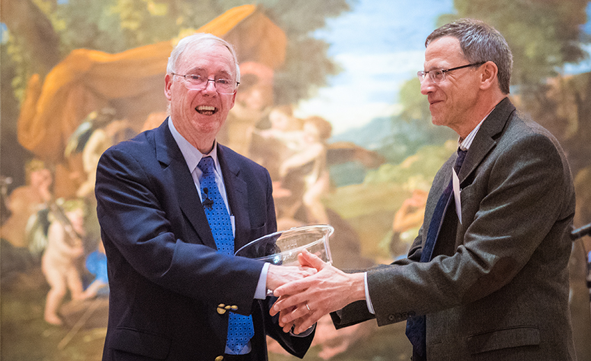 Two smiling men in suits hold a glass bowl