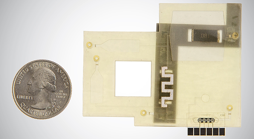 Close-up view of a flat, plastic-looking device with many square angles, an opening in the center, and a microfluidic strip. It is about 4 times the size of a quarter coin shown to the side.