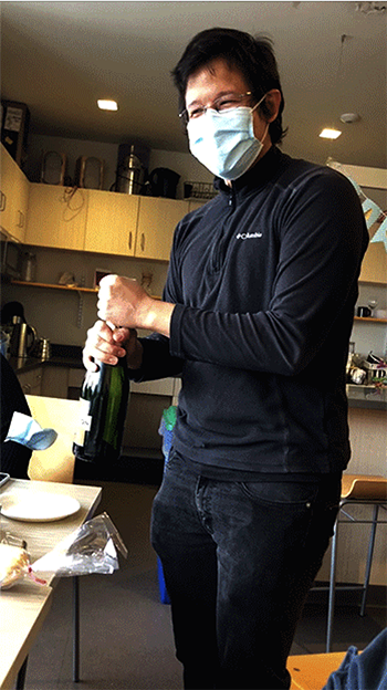 A man in a mask holds a champagne bottle in a lab