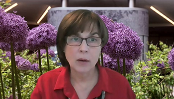 Screen shot of woman with short dark hair in front of a virtual background with flowers