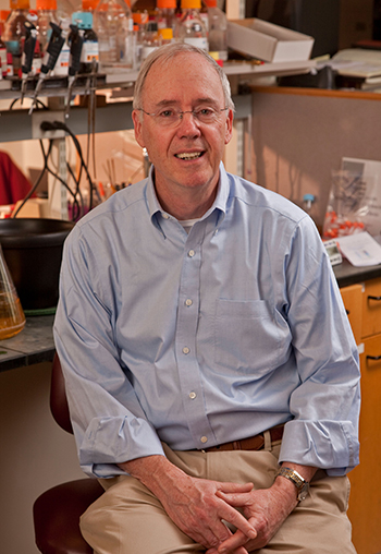 Portrait of a slightly smiling man seated in front of a lab bench