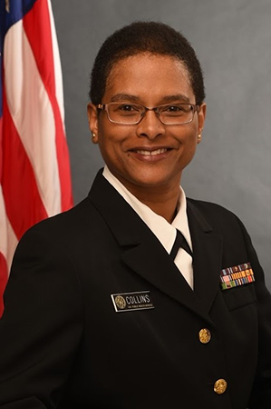 Portrait of RADM Felicia Collins wearing a uniform standing in front of the American Flag.